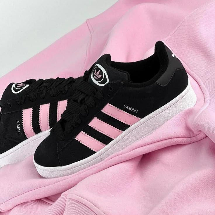 Black Adidas sneakers with pink accents on a pink fabric background
