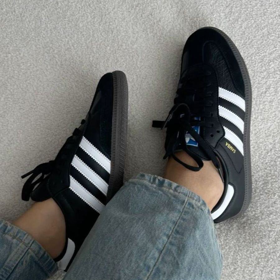 Black Adidas sneakers with white stripes worn with light blue jeans on a neutral background