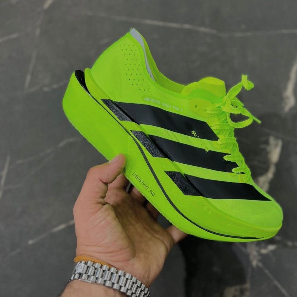 Bright green Adidas sneaker with black stripes held by a hand against a dark background