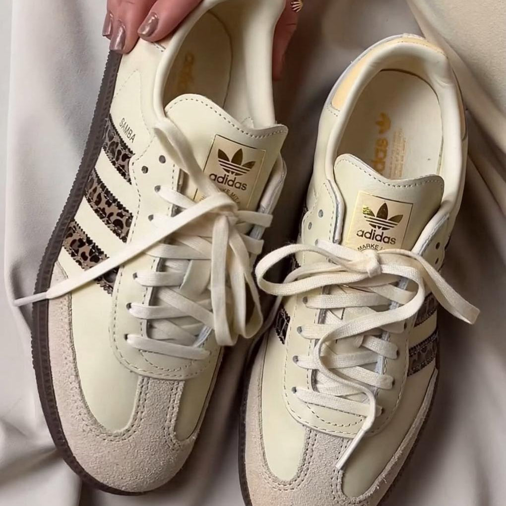 Pair of beige Adidas sneakers held by a hand on a light background