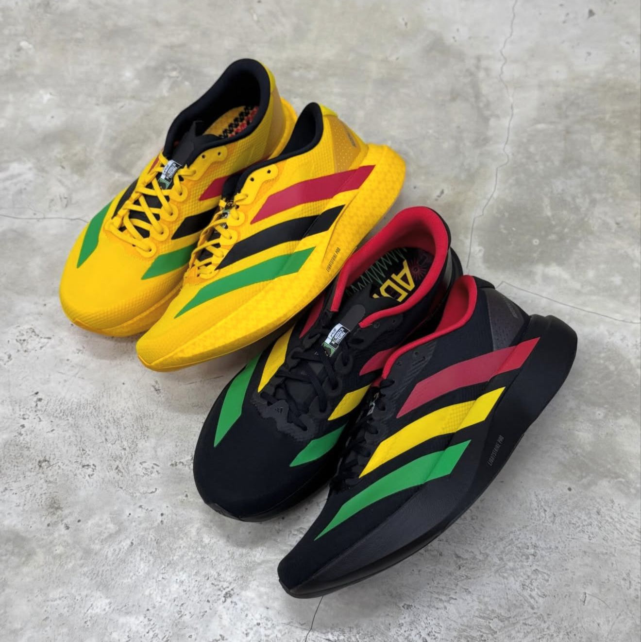 Pair of Adidas sneakers with yellow, black, red, and green color scheme on a concrete floor.