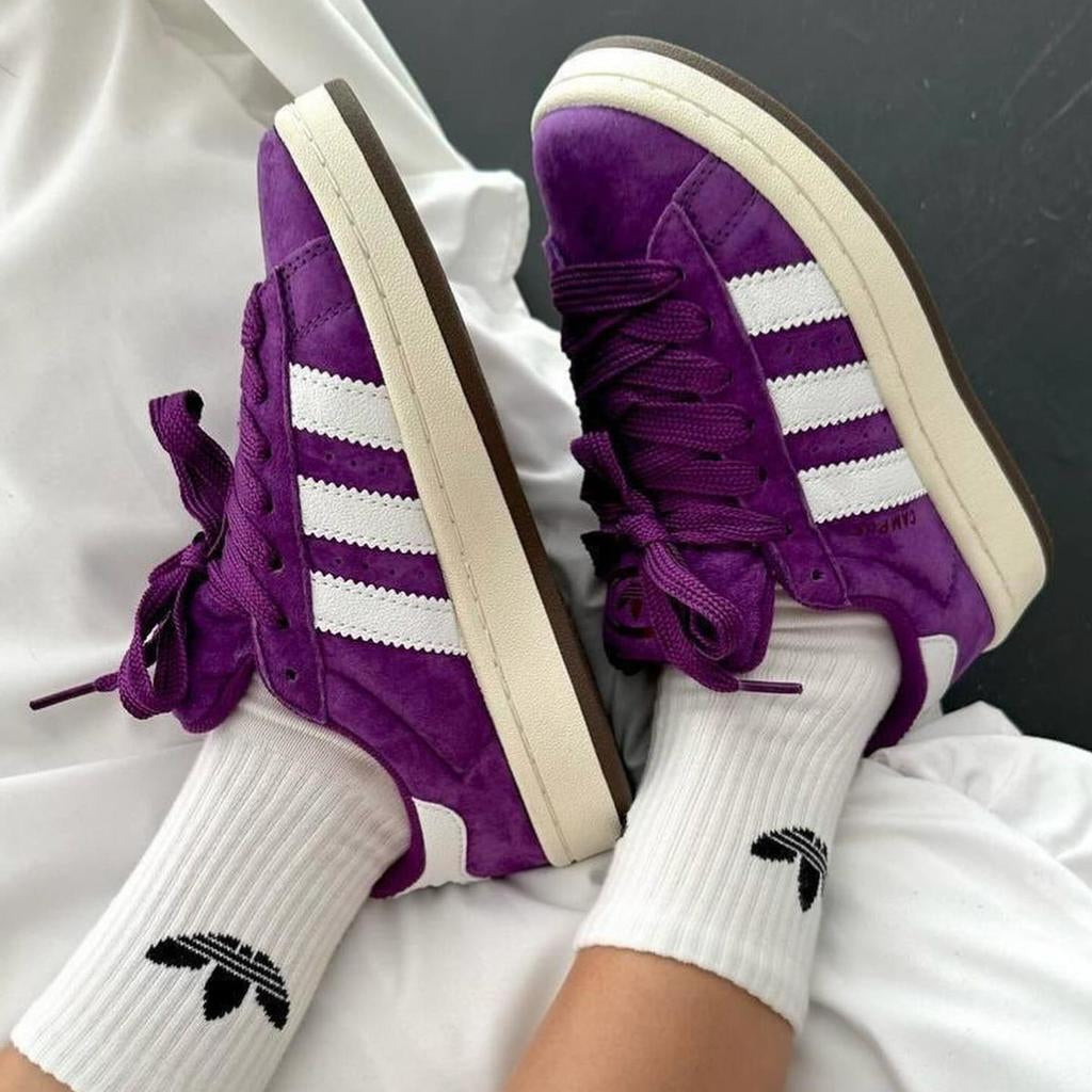 Purple Adidas sneakers with white stripes worn with white socks featuring Adidas logo.