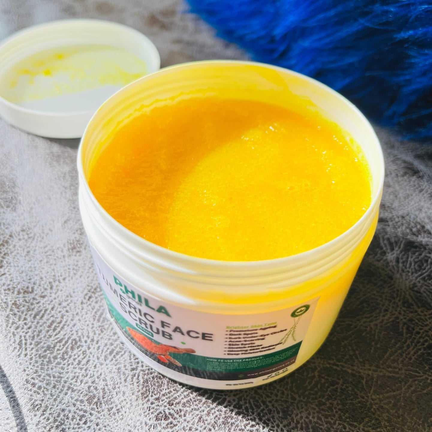 Turmeric face scrub in a container with a blue scrubber in the background