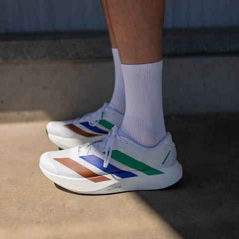 White adizero Evo SL sneakers with colorful stripes worn by a person on a concrete surface.