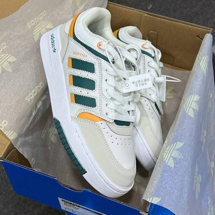 White Adidas sneaker with green and orange accents on a cardboard box.