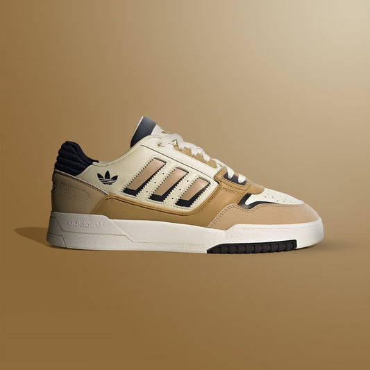 Beige Adidas sneaker with black accents on a brown background