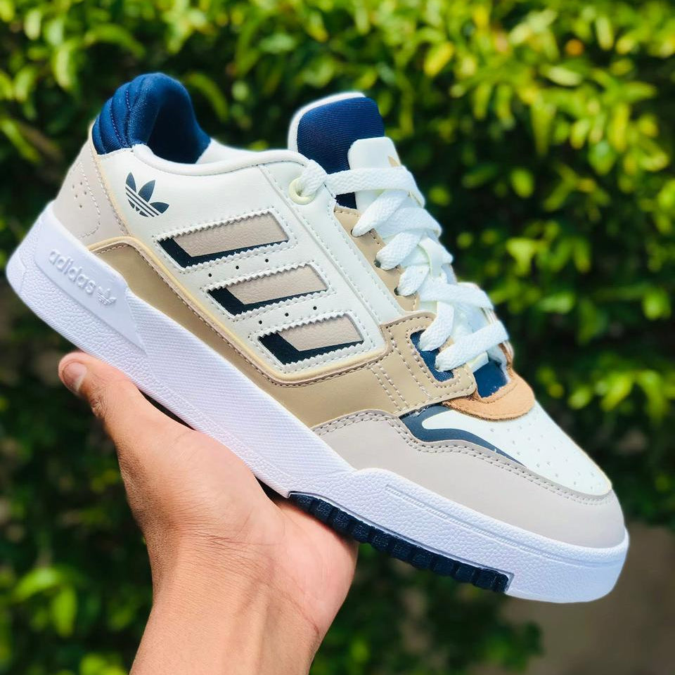 Beige and blue Adidas sneaker held in front of green foliage