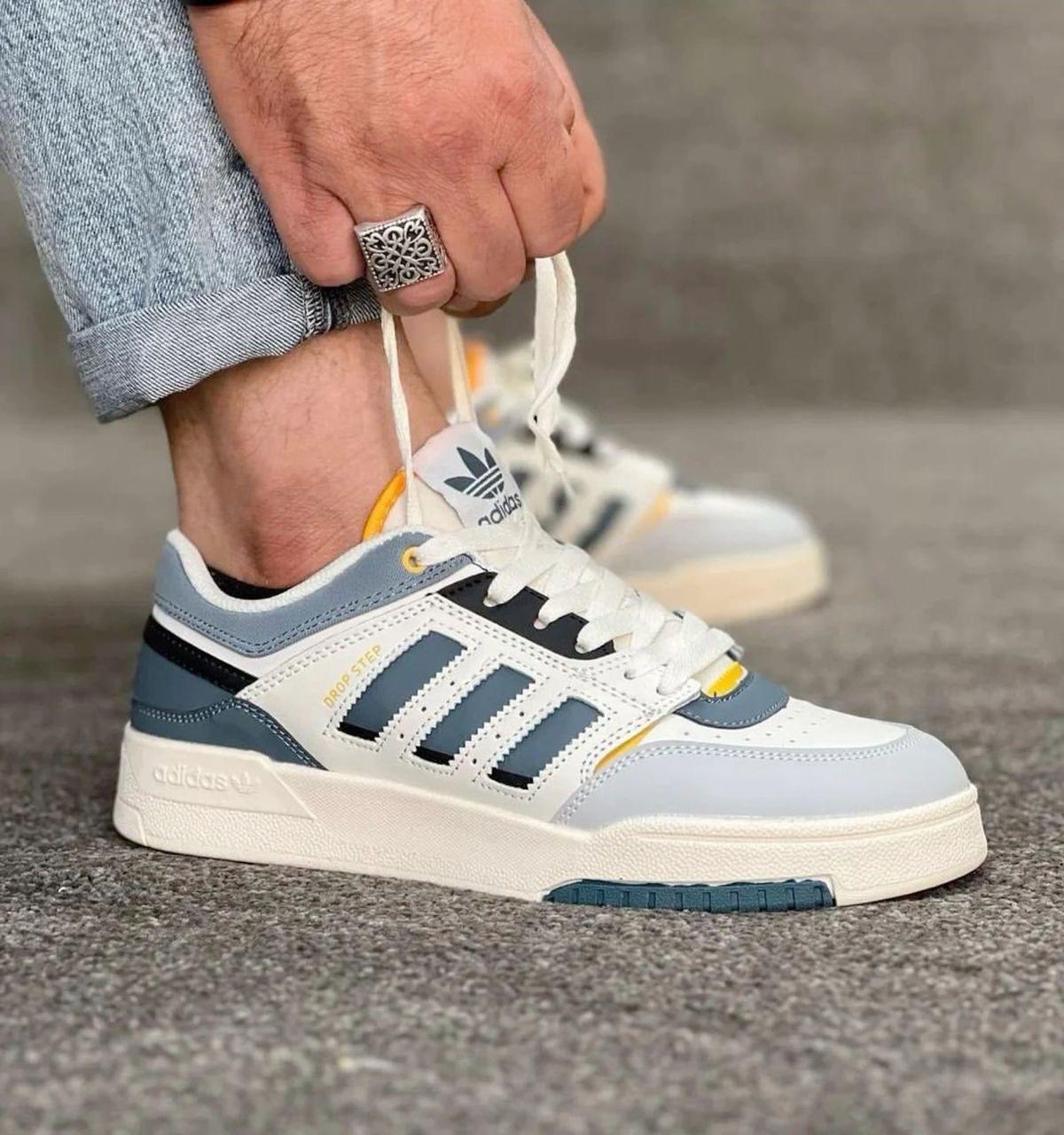 Person wearing a blue and white Adidas sneaker on a gray surface