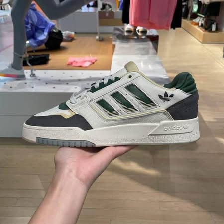 Adidas sneaker held in a hand with a store background