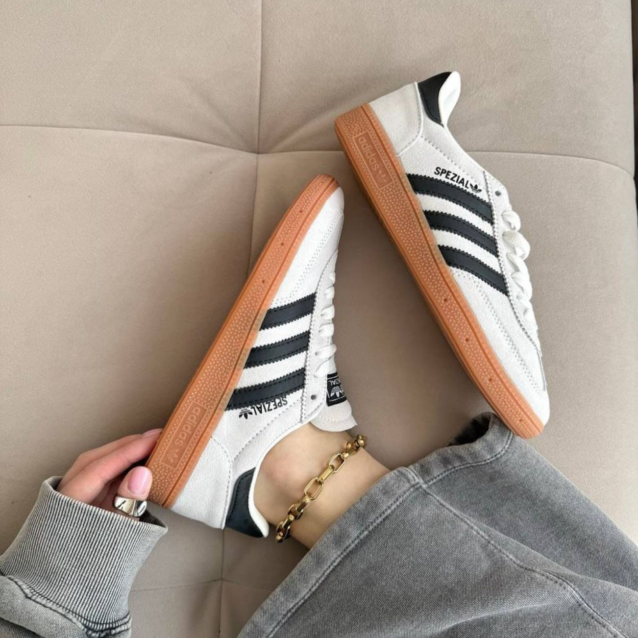Person wearing Adidas sneakers with black stripes on a beige couch